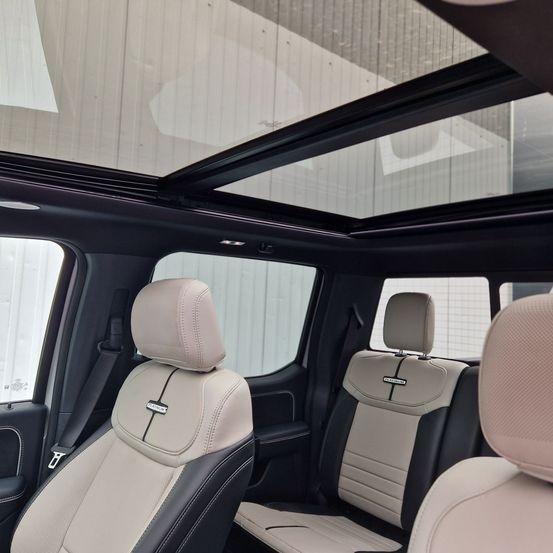 Innenraum eines Fahrzeugs mit beigefarbenen Ledersitzen mit schwarzen Akzenten und einem Schiebedach. Die Sitze sind mit Kopfstützen ausgestattet. Die Rücksitze haben ein Platinum-Emblem.