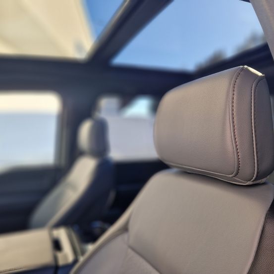 Eine Nahaufnahme eines beigen Ledersitzes mit einem Sonnendach oben, mit einem unscharfen Hintergrund des Autoinnenraums und des Himmels.