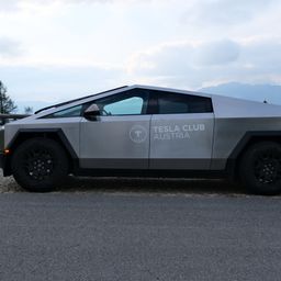 Ein silbernes Tesla Club Austria Fahrzeug mit futuristischem Design steht auf einem Kopfsteinpflasterweg mit Bergen im Hintergrund.