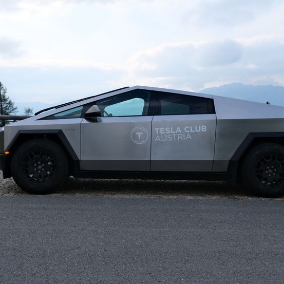 Ein silbernes Tesla Club Austria Fahrzeug mit futuristischem Design steht auf einem Kopfsteinpflasterweg mit Bergen im Hintergrund.