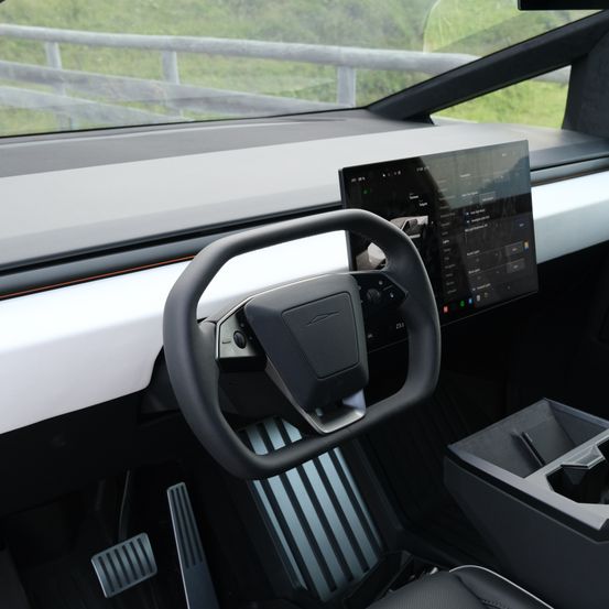 Innenansicht eines futuristischen Autos mit Lenkrad, Armaturenbrett mit Touchscreen-Display, Pedalen und einem Getränkehalter.