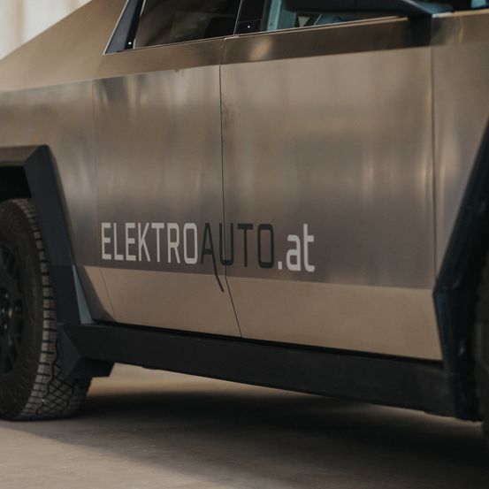 Ein metallisches Auto mit schlankem Design steht in einer Garage. Das Auto hat einen schwarzen Reifen und ein Logo mit der Aufschrift ELECTROAUTO.at an der Seite.
