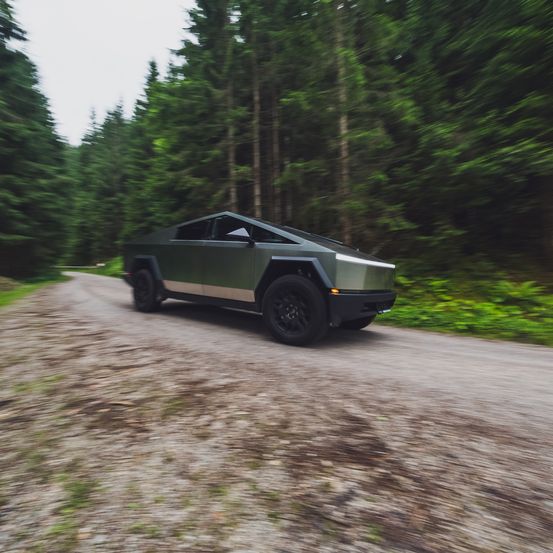 Ein schlanker, grüner SUV fährt auf einer schmalen, unbefestigten Straße, umgeben von hohen Bäumen. Der SUV hat ein niedriges Profil und ist aufgrund seiner hohen Geschwindigkeit verschwommen.
