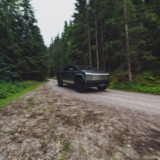 Ein schwarzer SUV fährt auf einer Schotterstraße, umgeben von hohen Bäumen in einem Wald.