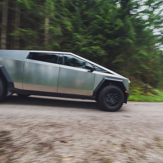Ein schlankes, silbernes, futuristisches Fahrzeug fährt auf einer unbefestigten Straße mit Waldhintergrund und fängt Bewegungsunschärfe ein.
