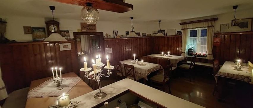 Ein gemütliches, kerzenbeleuchtetes Esszimmer mit Holzwänden und Tischen, Stühlen und Dekorationsartikeln. Der Raum ist schwach beleuchtet und schafft eine warme Atmosphäre.