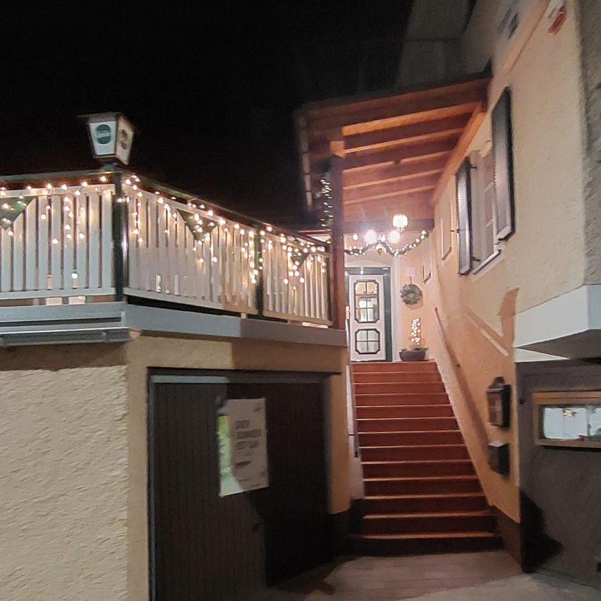 Ein Gebäude mit einem Balkon, beleuchtet von Weihnachtslichtern, einer Treppe, die zum Eingang führt, und einer Lampe an der Wand.