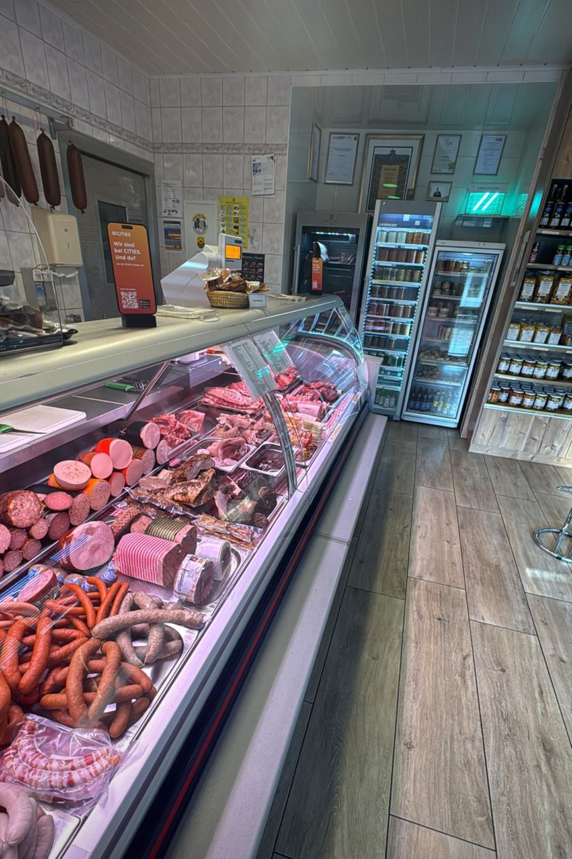 Ein Metzgerladen mit einer Vitrine voller verschiedener Fleisch- und Wurstsorten, zusammen mit anderen Produkten im Hintergrund.