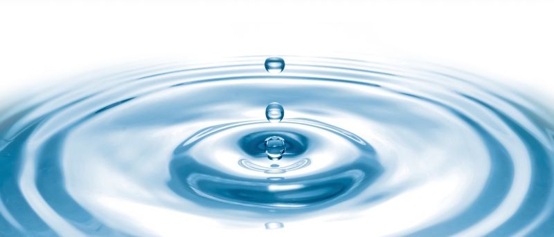 Drei Wassertropfen erzeugen Wellen in einer klaren blauen Flüssigkeit, wobei sich konzentrische Kreise nach außen ausbreiten.