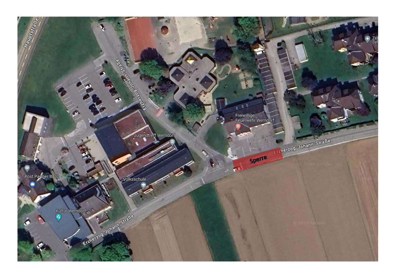 Eine Luftaufnahme von Werndorf zeigt Gebäude, einen Parkplatz und eine Straße. Ein rotes Schild sagt 'Sperre'.