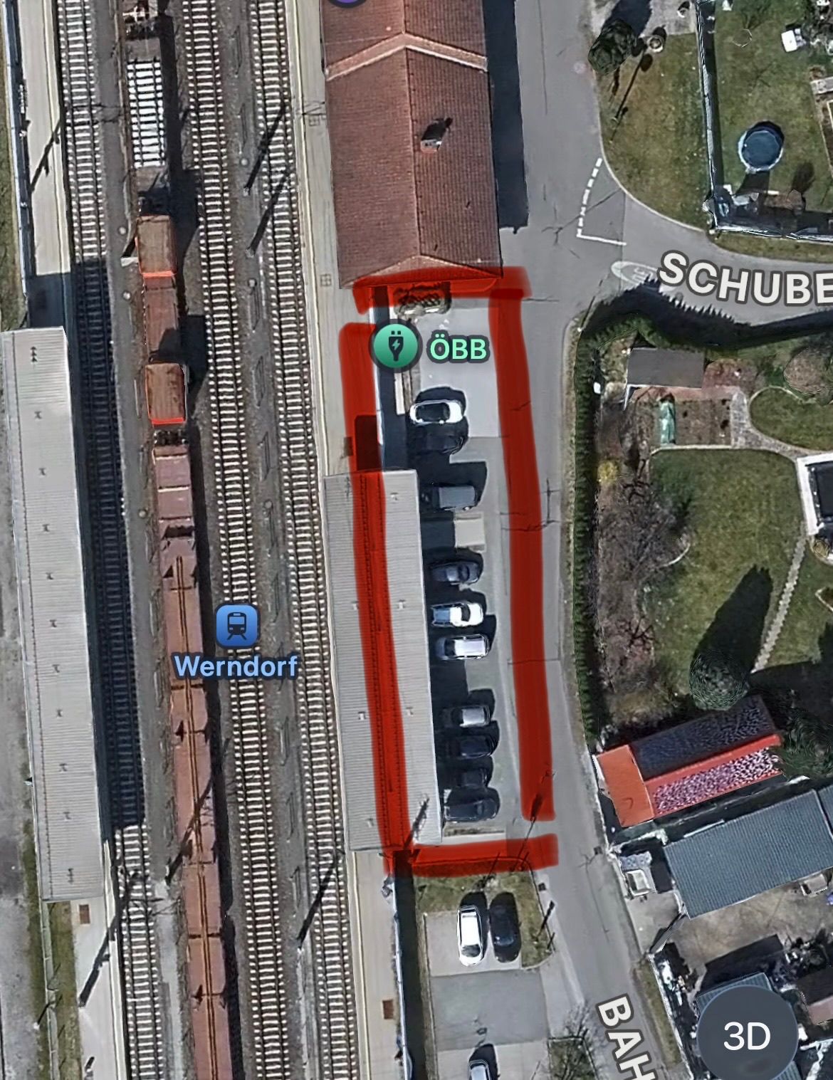 Eine Luftaufnahme von Werndorf mit einer Eisenbahnlinie und einer Straße. Die Eisenbahn ist mit einem Zugsymbol gekennzeichnet, und die Straße hat ein Gebäude mit einer roten Umrandung und dem Text OBB. Das Gebäude hat einen blauen Kreis mit einem weißen Symbol.
