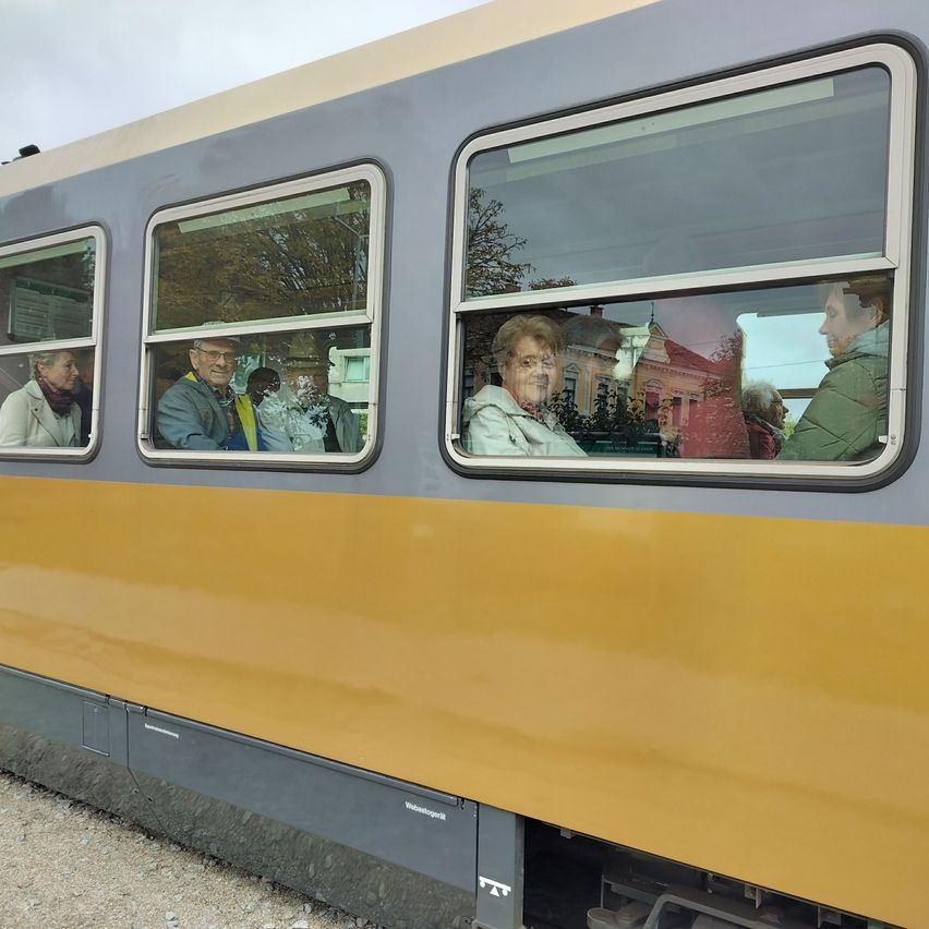 Einige Passagiere befinden sich in einem gelben und grauen Zug. Sie schauen aus den Fenstern auf die Außenansicht.