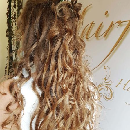 Eine Frau mit langen, blonden, gewellten Haaren, die in lockere Locken gestylt und mit einem Blumenhaaraccessoire geschmückt sind.