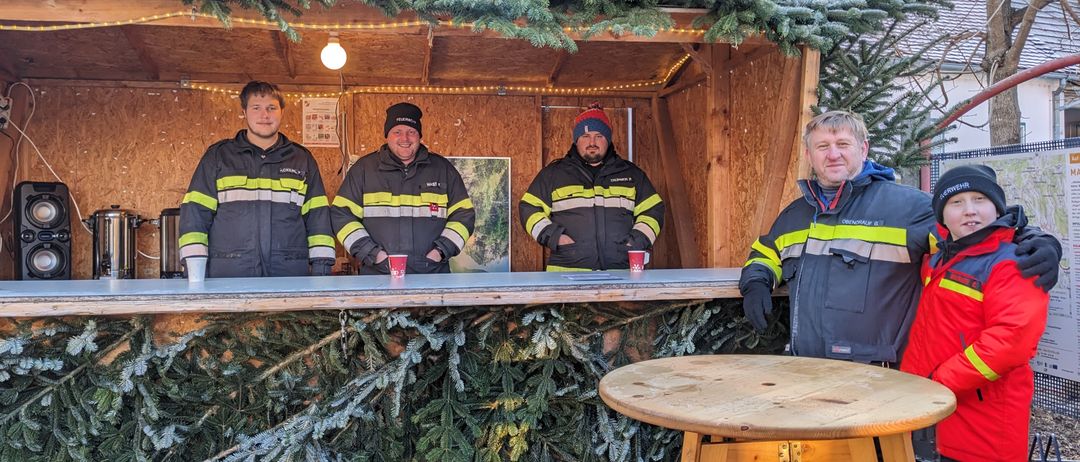Vier Feuerwehrleute in Uniformen stehen vor einer dekorierten Hütte mit roten Bechern auf der Theke.