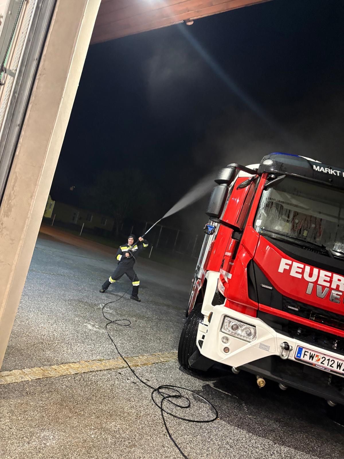 Ein Feuerwehrmann sprüht einen roten Feuerwehrwagen mit einem Schlauch bei Nacht auf einer Straße.