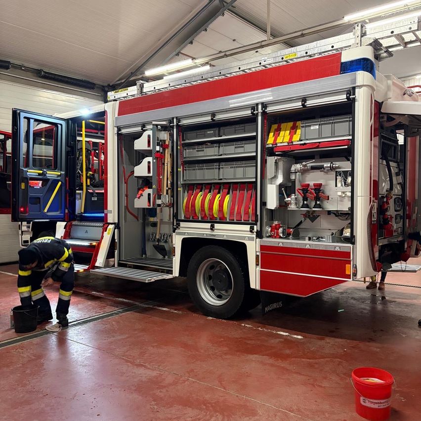 Ein Feuerwehrmann reinigt das Innere eines Feuerwehrwagens mit Werkzeug und Ausrüstung, die im Inneren der offenen Fahrzeugtüren sichtbar sind.