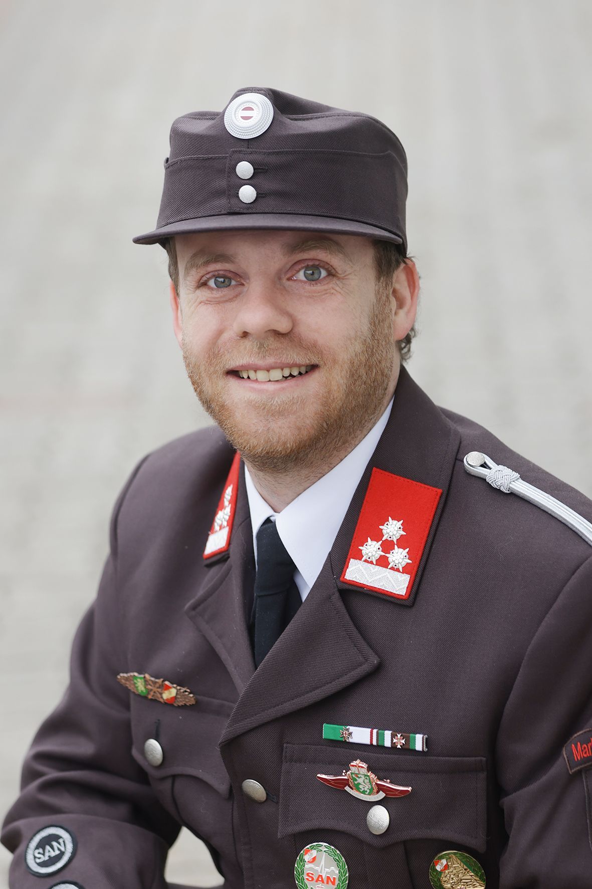 A man in a military uniform with a red patch on his shoulder and a black hat with white buttons.