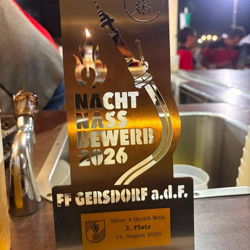 A golden plaque with a torch and flame design, reading 'NACHT NAS BEWERIB 2026' and 'FF GERSDORF a.d.F.' with a yellow label below stating 'Silber A Bezirk Weiz 2. Platz 14. August 2026'.