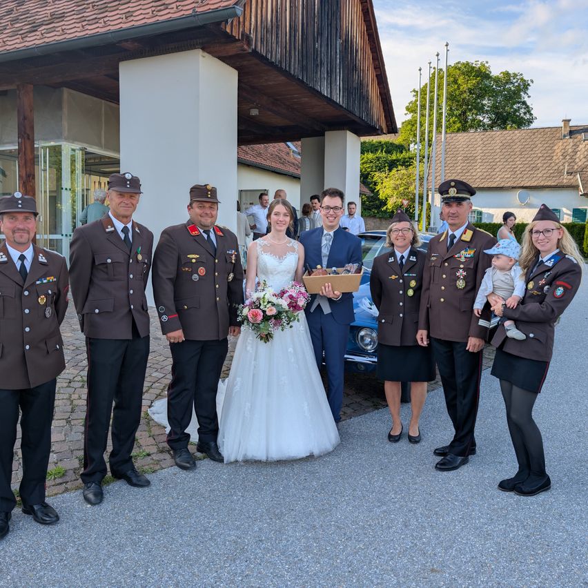 A newlywed couple with a baby and military personnel pose for a photo in front of a building.