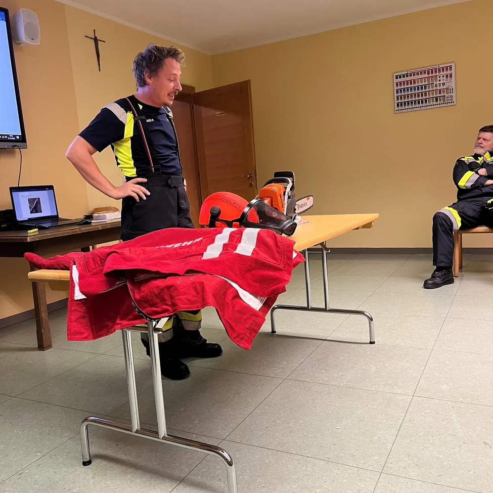 Ein Mann in einer Feuerwehruniform steht in einem Raum mit einem Tisch und einem Laptop.