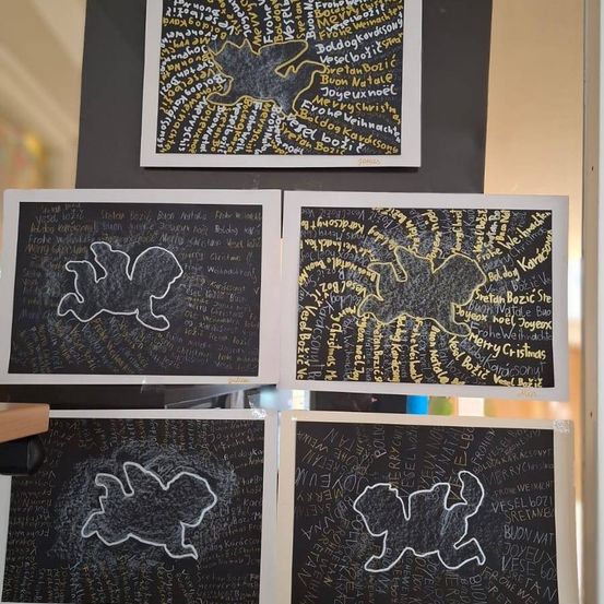 Vier gerahmte Drucke hängen an einer Wand, jeweils mit schwarzem Hintergrund und weißen Umrissen. Der obere linke Druck zeigt eine stilisierte Zeichnung eines Vogels. Der obere rechte Druck enthält Text und eine Zeichnung eines Vogels. Der untere linke Druck hat Text mit dem Umriss eines Vogels. Der untere rechte Druck zeigt einen Vogel und etwas Text.