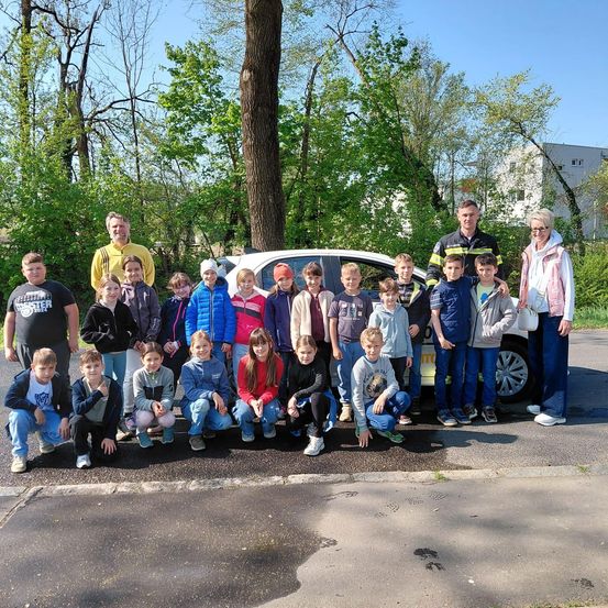 Eine Gruppe von Kindern und Erwachsenen posiert für ein Foto vor einem gelben Auto mit einem Polizisten und einer Frau.