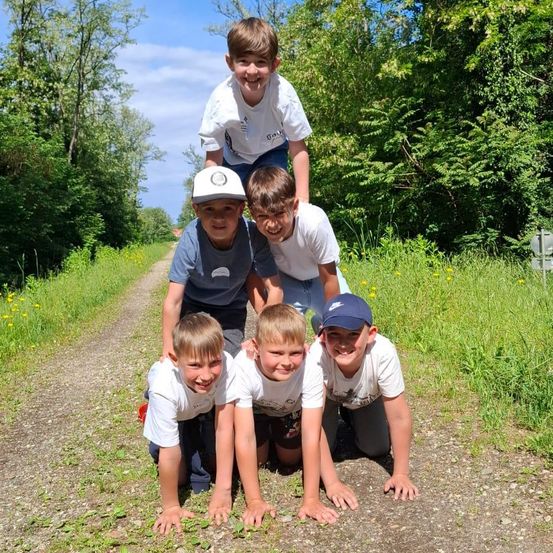 Fünf junge Jungen posieren für ein Foto auf einem Feldweg, wobei ein Junge auf den Schultern der anderen steht. Sie alle lächeln und scheinen Spaß zu haben.