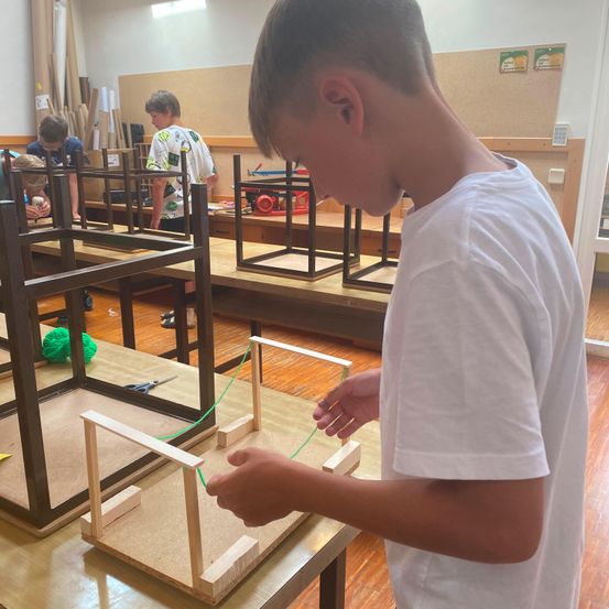 Ein Junge in einer Werkstatt arbeitet an einer Holzstruktur, während andere Schüler im Hintergrund an ähnlichen Projekten arbeiten.