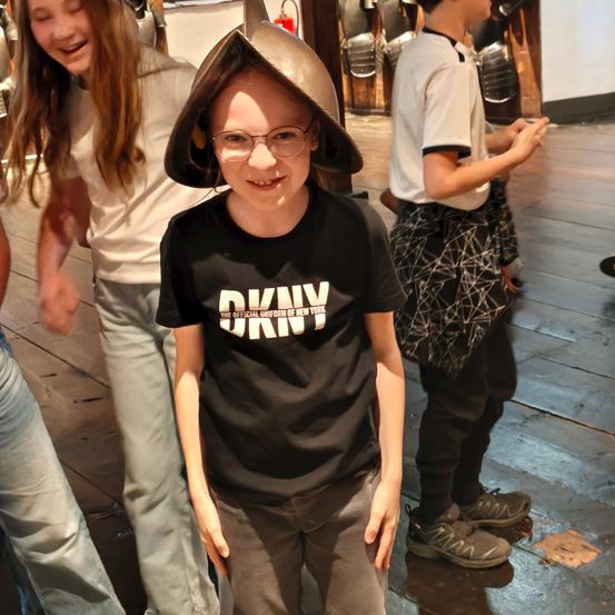 Ein junger Junge mit einem Metallhut und einer Brille steht neben einem Mädchen und einem Jungen in einem Museum.