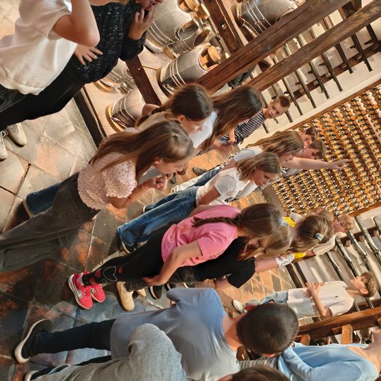 Eine Gruppe von Kindern versammelt sich in einem Raum, einige schauen auf einen Fass an der Wand, andere schauen nach unten.