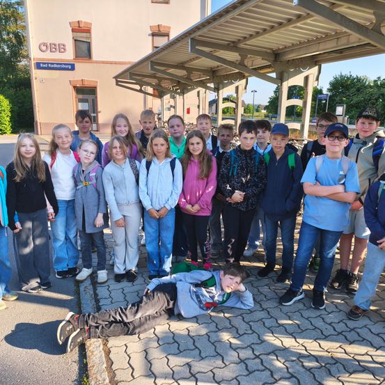 Eine Gruppe von Kindern und Jugendlichen posiert für ein Foto am Bahnhof, wobei ein Junge auf dem Boden liegt.