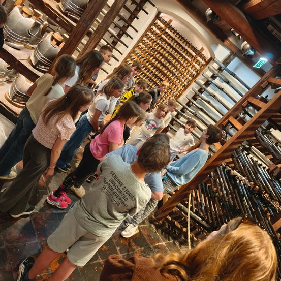 Eine Gruppe von Kindern ist in einem Museum versammelt und betrachtet verschiedene historische Artefakte. Der Raum ist schwach beleuchtet, und die Kinder tragen Freizeitkleidung.