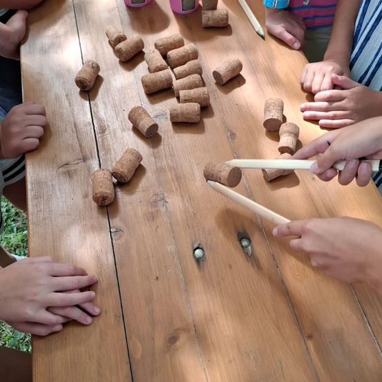 Eine Gruppe von Kindern spielt ein Spiel mit Holzstäben und Korken auf einem Holztisch.