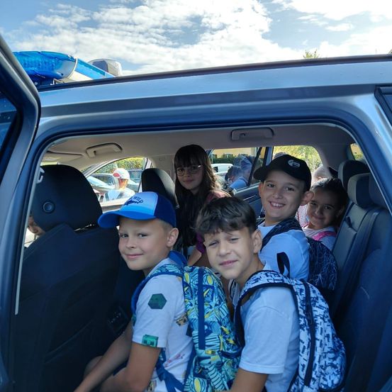 Eine Gruppe von Kindern mit Rucksäcken sitzt im hinteren Teil eines Polizeiwagens und lächelt für ein Foto.