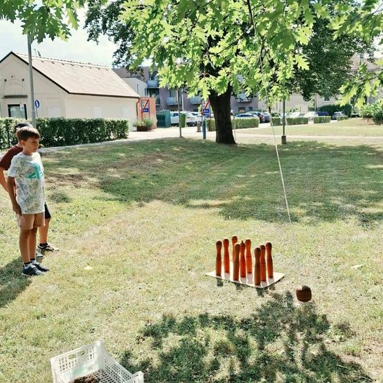Zwei Kinder stehen in einem Park und beobachten ein Spiel des Rasenbowlings. Das Spiel ist auf einem Rasenfeld mit einer Reihe von Holzkegeln aufgebaut.