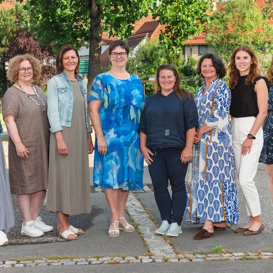 Eine Gruppe von Frauen in verschiedenen Outfits steht zusammen auf einem Bürgersteig vor einem Baum.