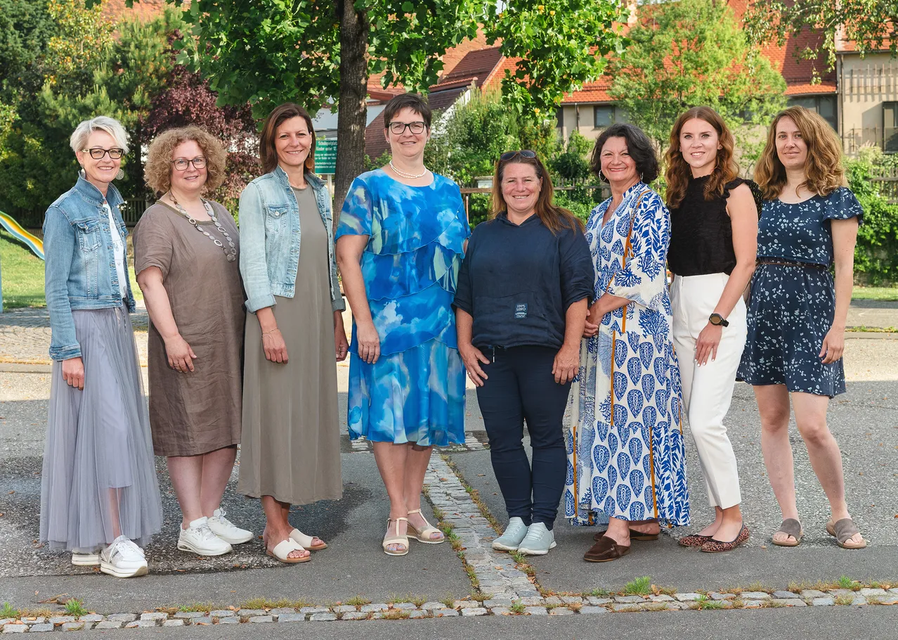 Eine Gruppe von Frauen in verschiedenen Outfits steht zusammen auf einem Bürgersteig vor einem Baum.