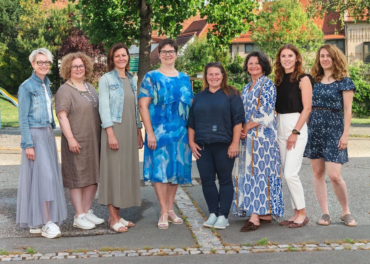 Eine Gruppe von Frauen in verschiedenen Outfits steht zusammen auf einem Bürgersteig vor einem Baum.