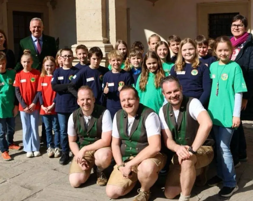 Gruppenfoto von Menschen in grünen und roten Shirts mit einem Mann im Anzug, der vor einem Gebäude lächelt.