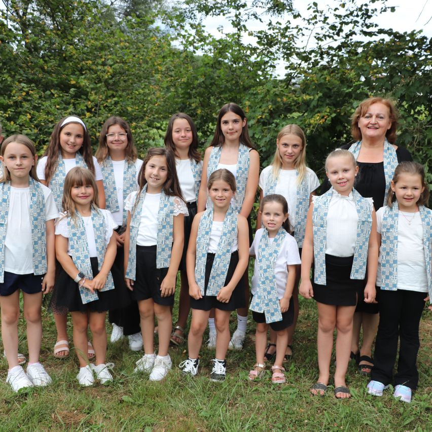 Eine Gruppe von Mädchen in passenden Uniformen posiert für ein Foto im Freien auf einer Grasfläche mit Bäumen im Hintergrund.