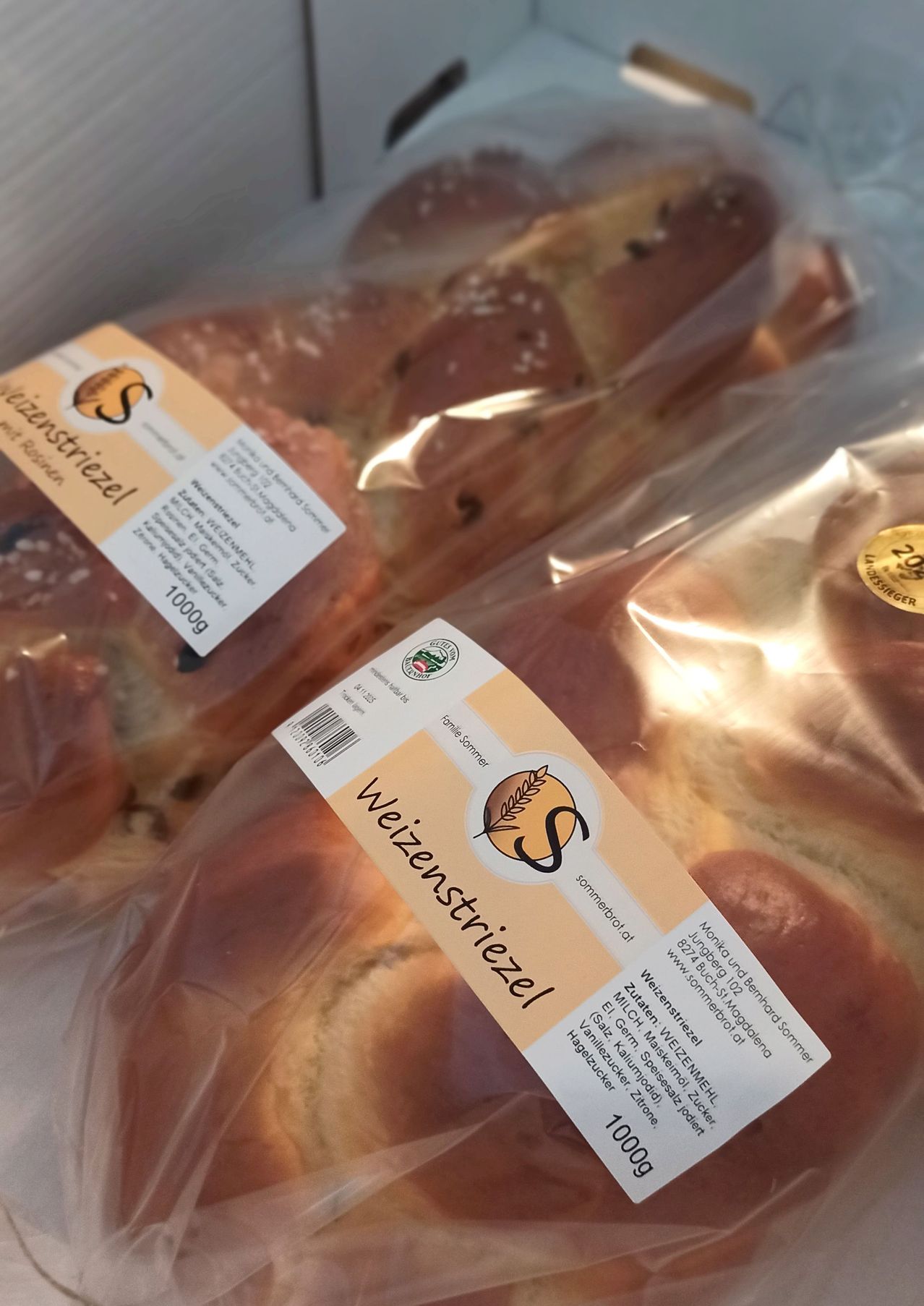 A close-up of packaged pastries, including bread rolls, likely sweet bread, with a focus on the label reading 'Weizenstreifel' and a logo. The rolls are wrapped in plastic, suggesting freshness and individual packaging.