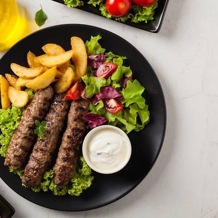 Ein Teller mit gegrilltem Fleisch mit einer Beilage Pommes und einem Salat auf einem Marmortisch.
