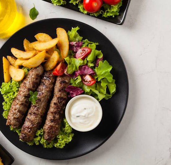 Ein Teller mit gegrilltem Fleisch mit einer Beilage Pommes und einem Salat auf einem Marmortisch.