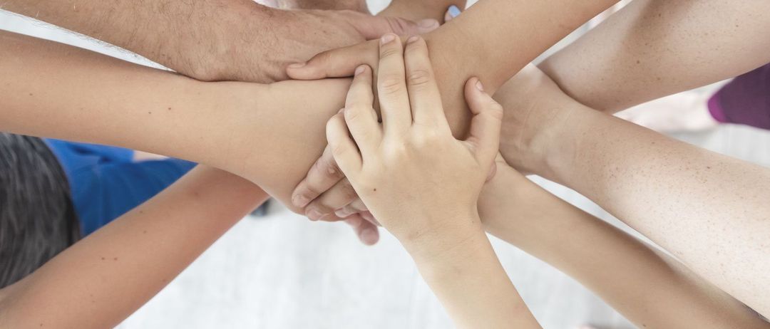 Eine Gruppe von Menschen, die in einem Kreis die Hände halten und Einigkeit und Teamarbeit zeigen.