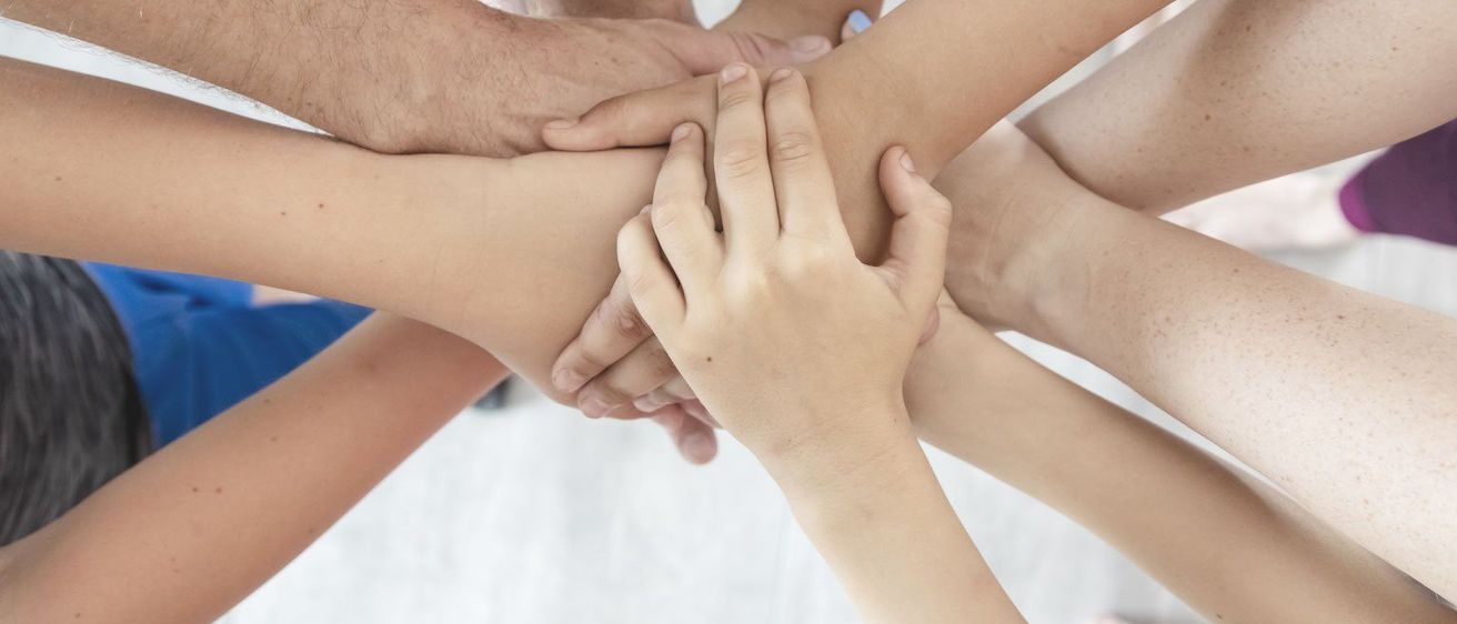 Eine Gruppe von Menschen, die in einem Kreis die Hände halten und Einigkeit und Teamarbeit zeigen.