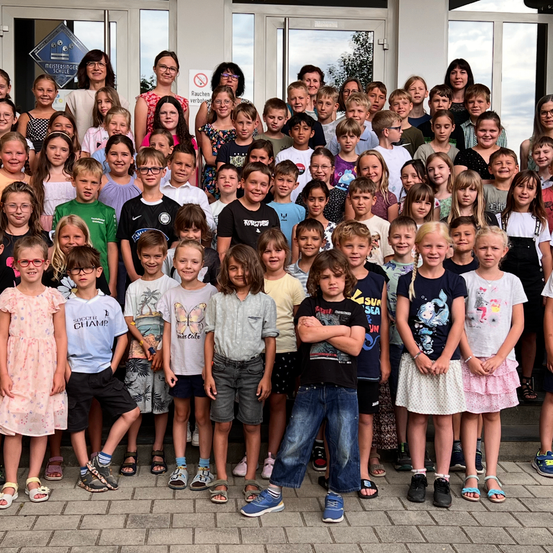 Eine Gruppe von Kindern und Erwachsenen vor einem Gebäude mit Glastüren, in verschiedenen Outfits und mit Accessoires.
