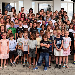 Eine Gruppe von Kindern und Erwachsenen vor einem Gebäude mit Glastüren, in verschiedenen Outfits und mit Accessoires.