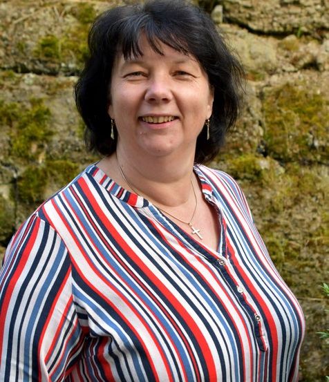Eine Frau mit einem rot, weiß und blau gestreiften Hemd steht vor einer Steinmauer.