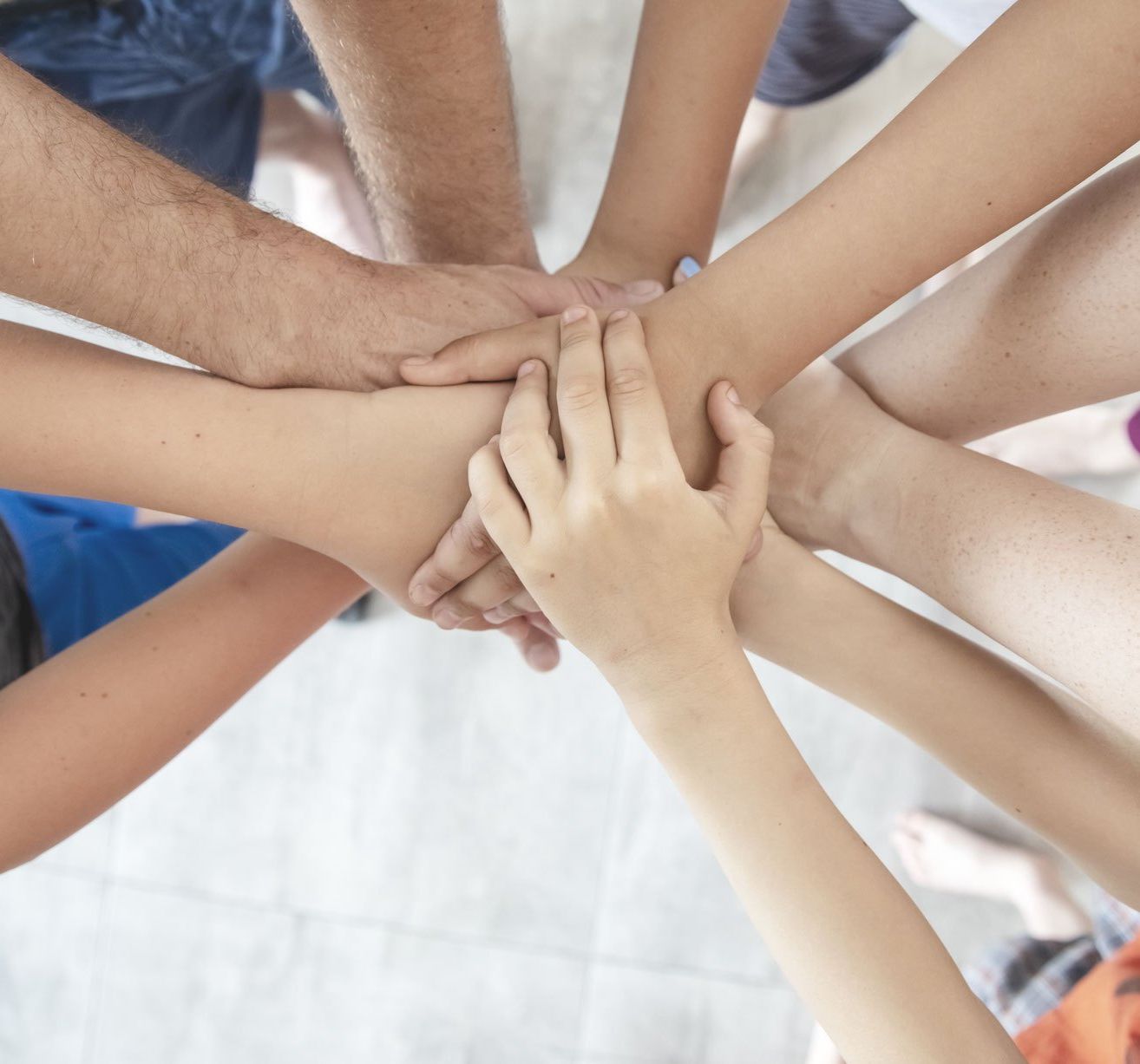 Mehrere Menschen unterschiedlichen Alters halten in einem Kreis die Hände, möglicherweise als Symbol für Einheit oder Unterstützung.
