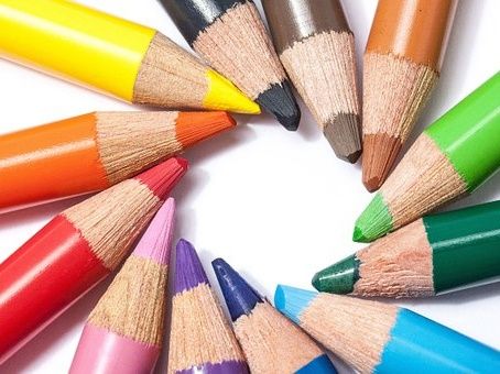 Eine Sammlung von Buntstiften, die in einem kreisförmigen Muster auf einem weißen Hintergrund angeordnet sind. Die Stifte haben verschiedene Farben, darunter Gelb, Orange, Rot, Pink, Lila, Blau, Grün und Braun.